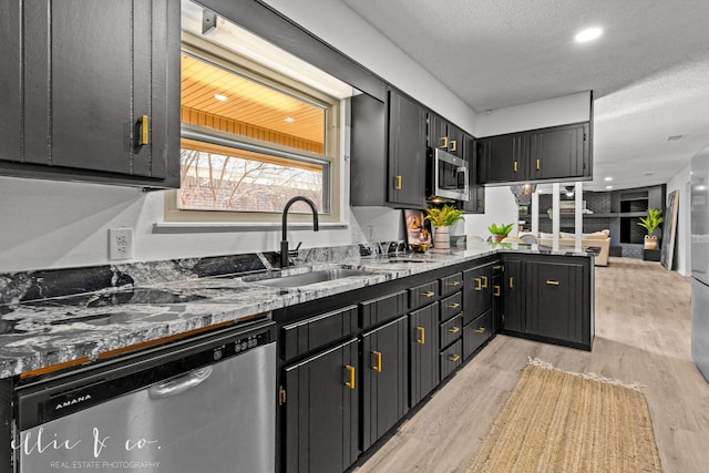 kitchen featuring a textured ceiling, stainless steel appliances, light hardwood / wood-style floors, sink, and stone counters