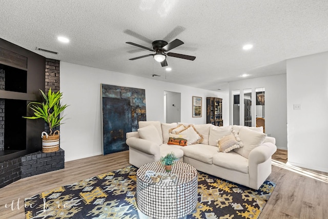 living room featuring a brick fireplace, hardwood / wood-style floors, a textured ceiling, and ceiling fan