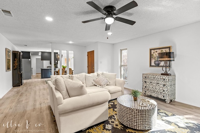 living room featuring light hardwood / wood-style floors, a textured ceiling, and ceiling fan