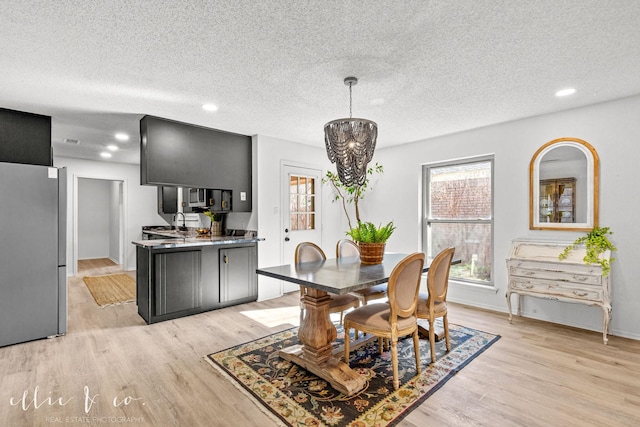 dining area featuring light wood-type flooring, an inviting chandelier, a textured ceiling, and sink