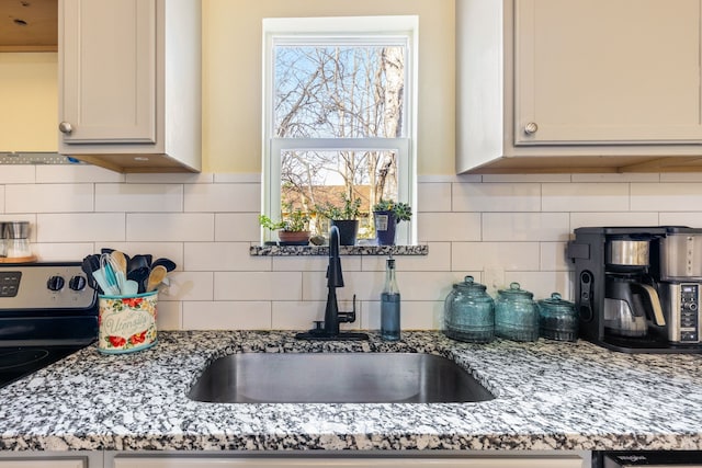 kitchen with light stone counters, tasteful backsplash, sink, and stainless steel range with electric cooktop