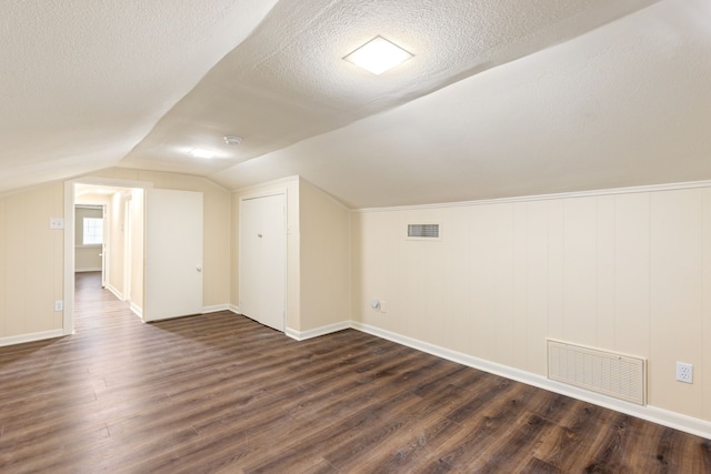 additional living space featuring dark wood-type flooring, lofted ceiling, and a textured ceiling