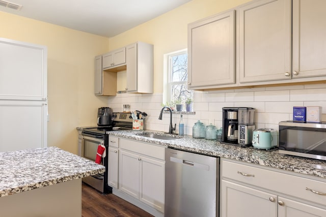 kitchen featuring sink, decorative backsplash, stainless steel appliances, light stone countertops, and dark wood-type flooring