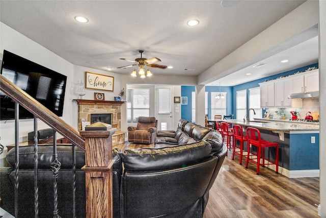 living room with sink, a fireplace, a textured ceiling, hardwood / wood-style floors, and ceiling fan with notable chandelier