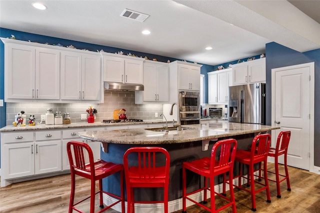 kitchen with stainless steel appliances, a center island with sink, light wood-type flooring, white cabinets, and sink