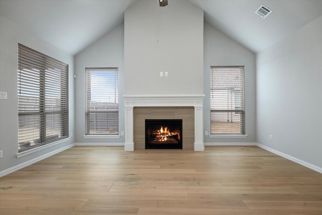 unfurnished living room featuring a fireplace, lofted ceiling, light hardwood / wood-style flooring, and a healthy amount of sunlight