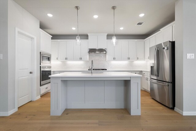 kitchen featuring decorative light fixtures, light hardwood / wood-style floors, stainless steel appliances, and an island with sink