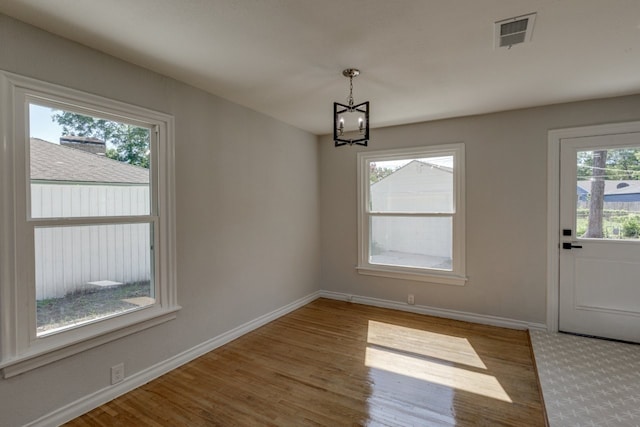 unfurnished dining area featuring a chandelier and wood-type flooring