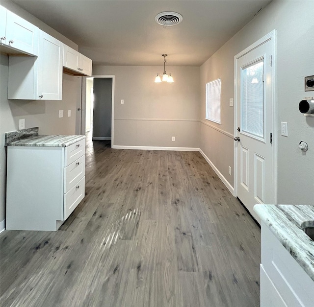 kitchen featuring white cabinets, hanging light fixtures, light stone countertops, an inviting chandelier, and light hardwood / wood-style flooring