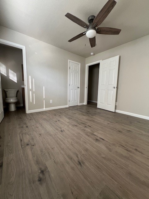 unfurnished bedroom with ensuite bathroom, dark hardwood / wood-style floors, and ceiling fan