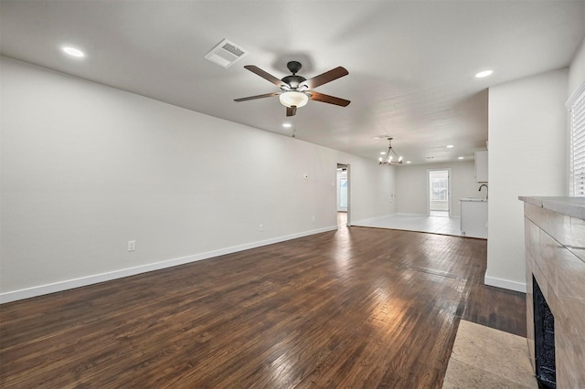 unfurnished living room featuring ceiling fan with notable chandelier, dark hardwood / wood-style flooring, and a fireplace