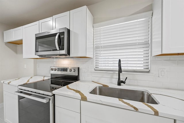 kitchen with light stone counters, sink, white cabinetry, and stainless steel appliances