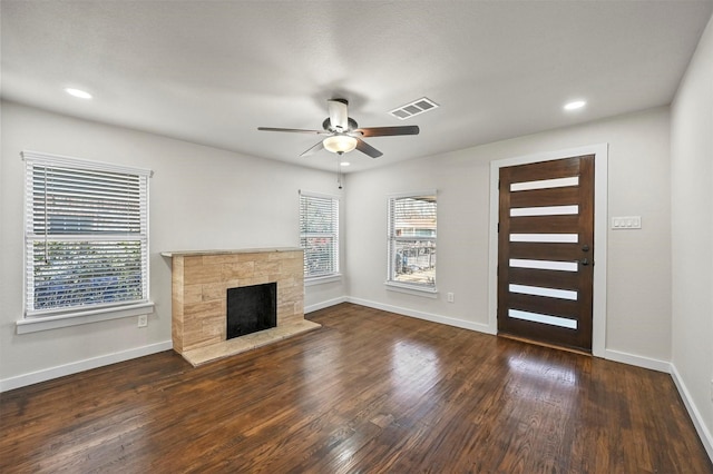 unfurnished living room featuring dark hardwood / wood-style floors, ceiling fan, and a stone fireplace