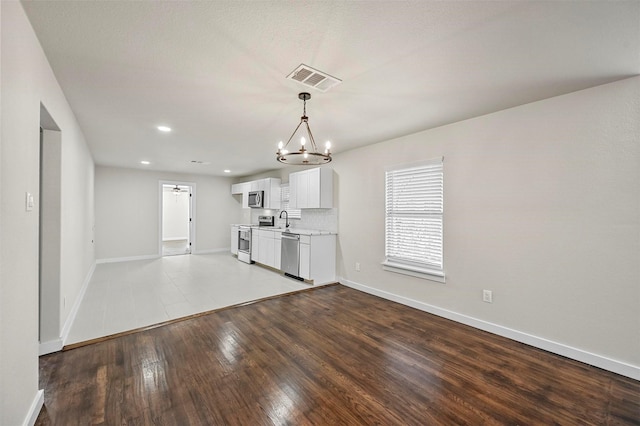 kitchen featuring hardwood / wood-style floors, sink, appliances with stainless steel finishes, a notable chandelier, and white cabinetry