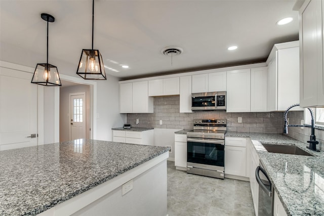 kitchen featuring hanging light fixtures, sink, appliances with stainless steel finishes, stone countertops, and white cabinetry