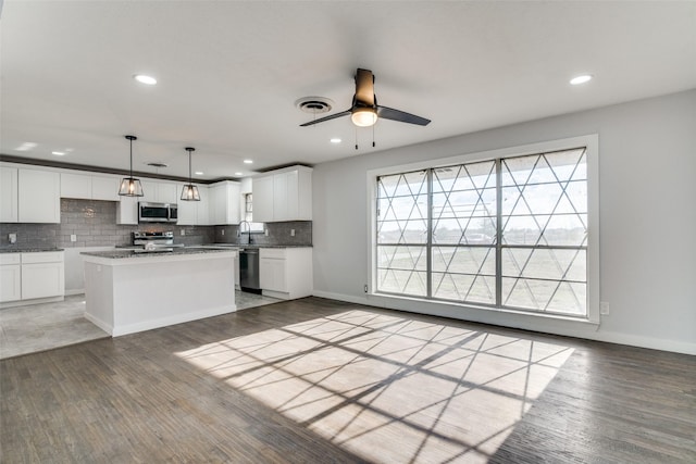 kitchen with a center island, hardwood / wood-style floors, decorative light fixtures, white cabinets, and appliances with stainless steel finishes