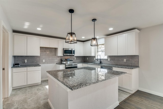 kitchen with appliances with stainless steel finishes, sink, white cabinets, a center island, and hanging light fixtures