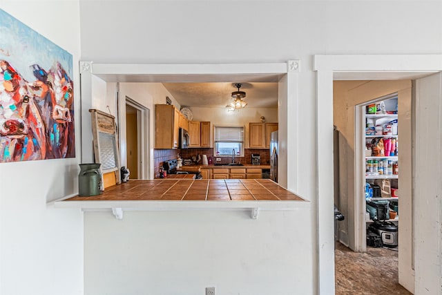 kitchen with a breakfast bar, appliances with stainless steel finishes, tasteful backsplash, tile counters, and kitchen peninsula