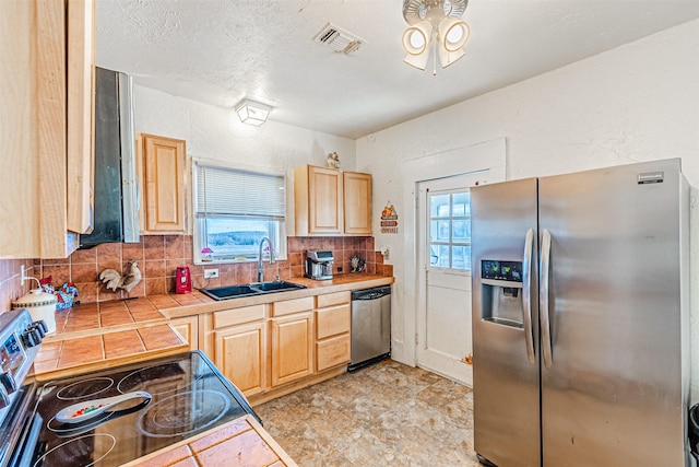 kitchen featuring decorative backsplash, light brown cabinetry, stainless steel appliances, sink, and tile counters