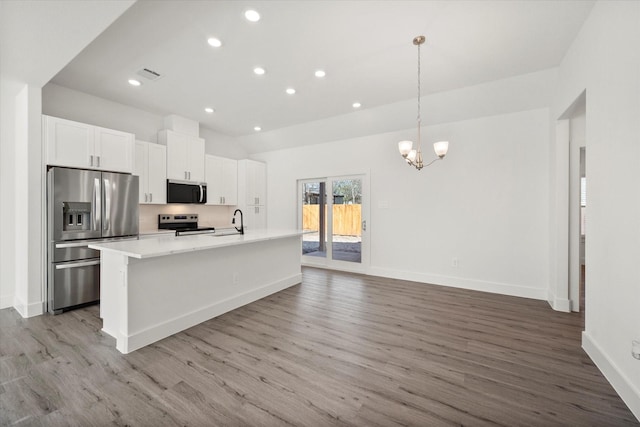 kitchen with hanging light fixtures, light hardwood / wood-style flooring, an island with sink, appliances with stainless steel finishes, and white cabinetry