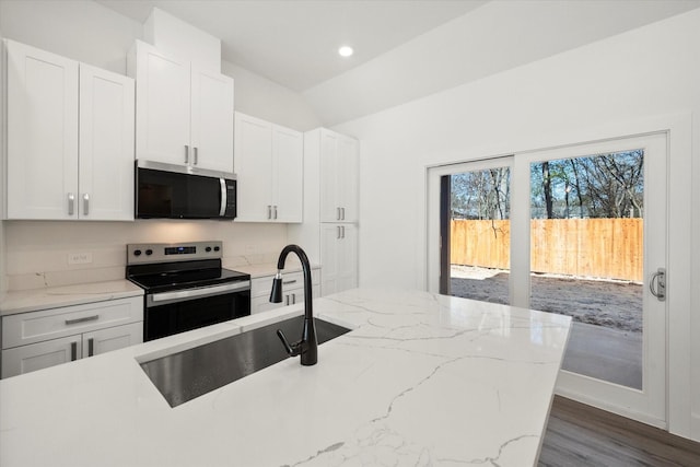 kitchen featuring light stone countertops, appliances with stainless steel finishes, vaulted ceiling, sink, and white cabinetry