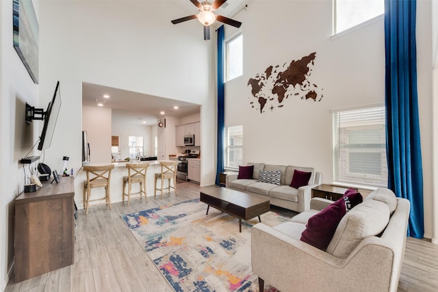 living room with a high ceiling, light hardwood / wood-style floors, and ceiling fan