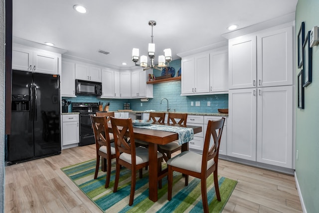 kitchen with white cabinets, light hardwood / wood-style flooring, hanging light fixtures, and black appliances