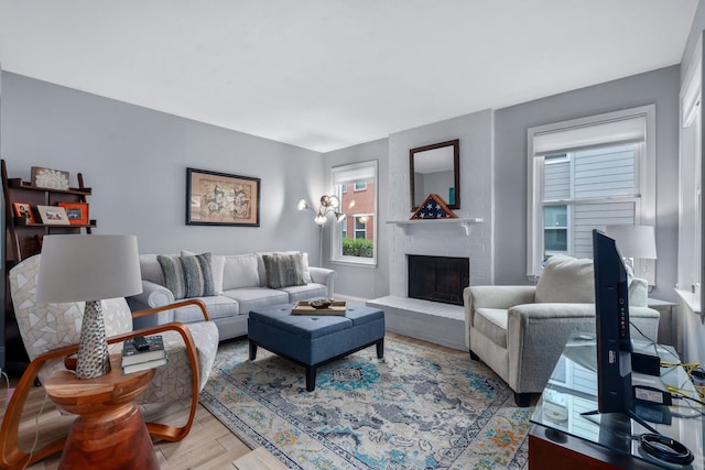 living area featuring light wood finished floors, a brick fireplace, and baseboards