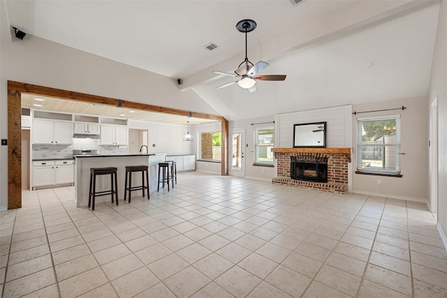 unfurnished living room featuring ceiling fan, lofted ceiling with beams, light tile patterned flooring, and a brick fireplace