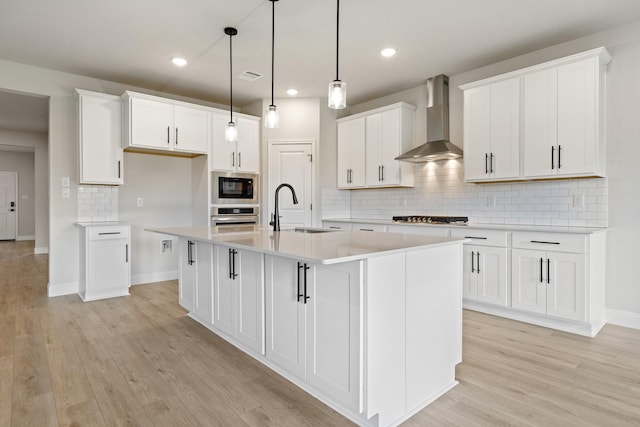 209 Briarwood Dr, Nevada, TX 75173 - kitchen featuring wall chimney range hood, stainless steel appliances, a kitchen island with sink, decorative backsplash, and white cabinets