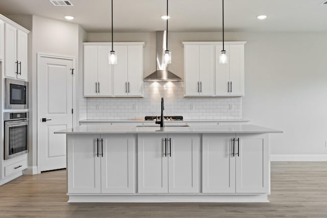 209 Briarwood Dr, Nevada, TX 75173 - kitchen featuring wall chimney range hood, stainless steel oven, an island with sink, white cabinetry, and light wood-style floors
