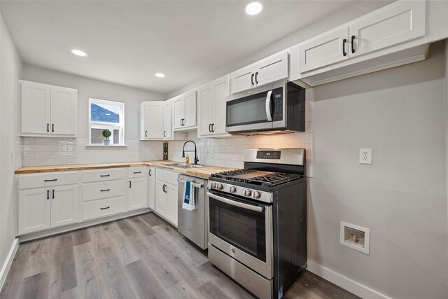 kitchen with butcher block counters, white cabinetry, sink, tasteful backsplash, and appliances with stainless steel finishes