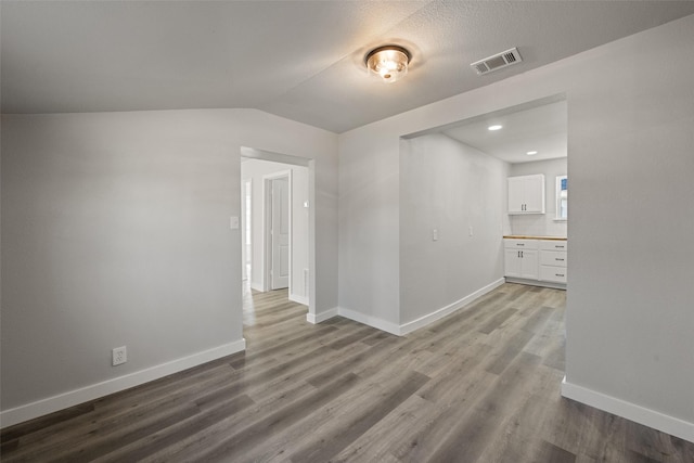 empty room with a textured ceiling, light wood-type flooring, and vaulted ceiling