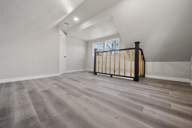 additional living space featuring a textured ceiling, light hardwood / wood-style floors, and vaulted ceiling