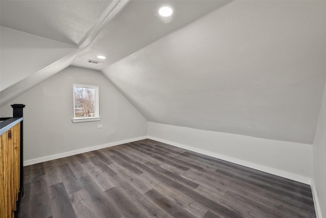 additional living space with vaulted ceiling, dark wood-type flooring, and a textured ceiling