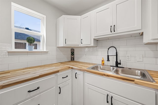 kitchen featuring butcher block countertops, decorative backsplash, white cabinetry, and sink