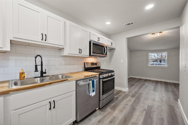 kitchen with wood counters, white cabinets, sink, decorative backsplash, and stainless steel appliances