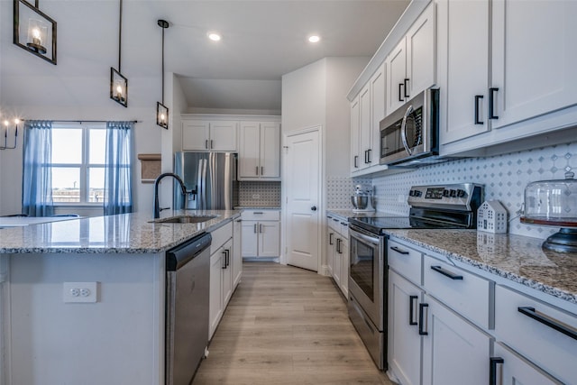 kitchen featuring a kitchen island with sink, stainless steel appliances, decorative light fixtures, decorative backsplash, and white cabinets