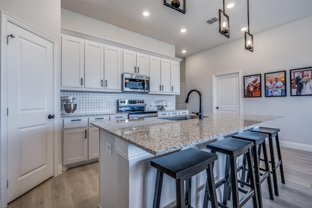 kitchen with white cabinets, appliances with stainless steel finishes, sink, and an island with sink