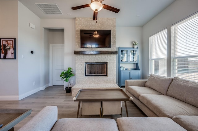 living room featuring ceiling fan, a fireplace, and light wood-type flooring