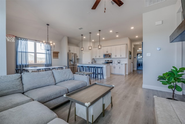 living room featuring ceiling fan with notable chandelier, sink, and light hardwood / wood-style flooring