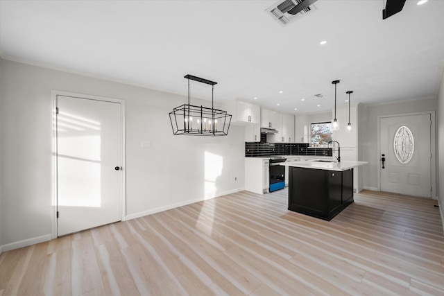 kitchen with pendant lighting, tasteful backsplash, white cabinetry, an island with sink, and light wood-type flooring