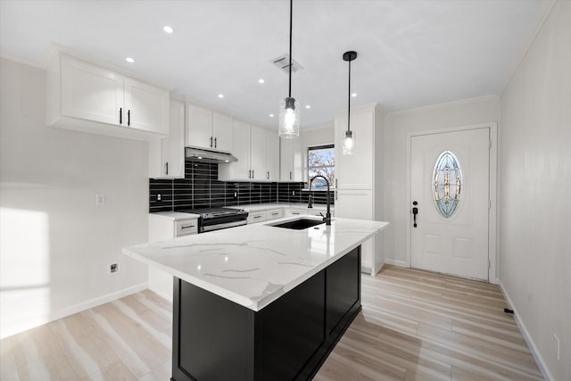 kitchen with pendant lighting, white cabinetry, sink, light stone countertops, and a center island with sink