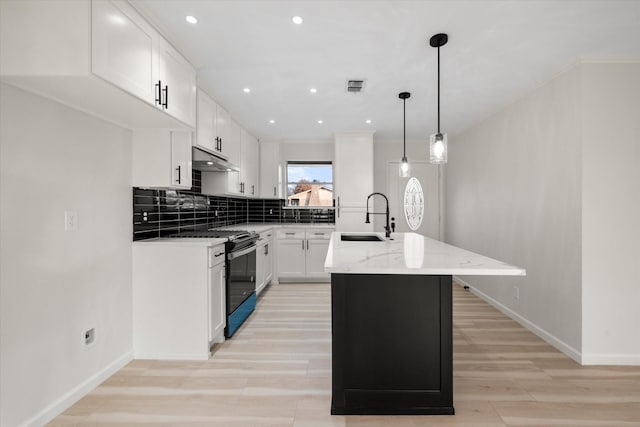 kitchen featuring stainless steel gas range, sink, light stone counters, a center island, and white cabinets