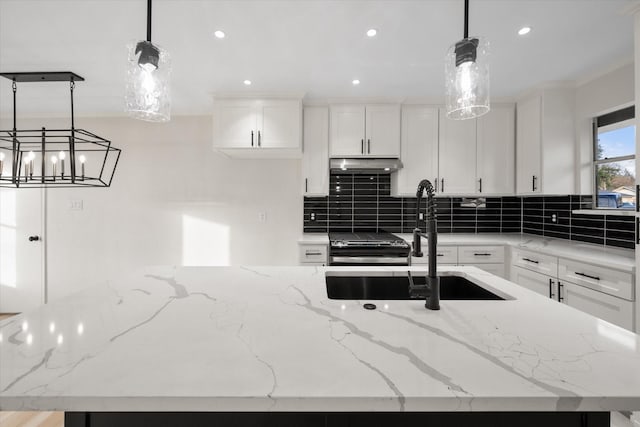 kitchen featuring pendant lighting, light stone counters, white cabinetry, and a center island with sink