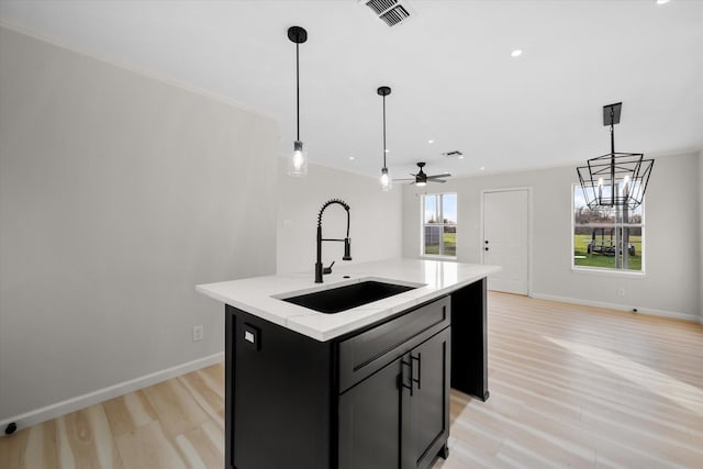 kitchen featuring sink, ornamental molding, a kitchen island with sink, pendant lighting, and light hardwood / wood-style floors