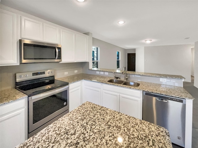 kitchen with white cabinets, appliances with stainless steel finishes, light stone countertops, and sink