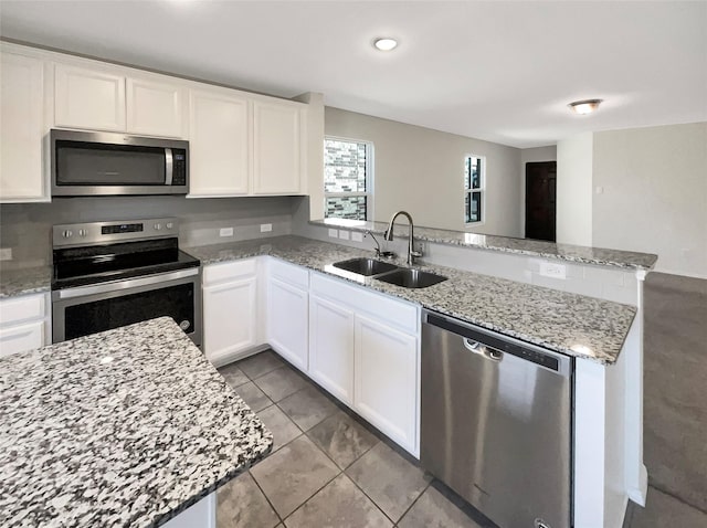 kitchen with appliances with stainless steel finishes, light stone counters, sink, white cabinets, and tile patterned flooring