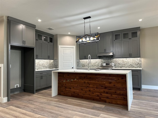 kitchen with backsplash, sink, decorative light fixtures, stainless steel stove, and an island with sink