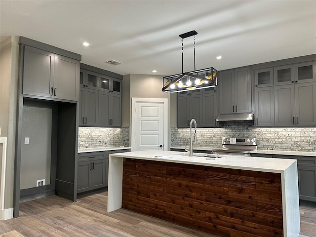 kitchen with stainless steel electric range oven, light stone counters, pendant lighting, a center island with sink, and hardwood / wood-style flooring